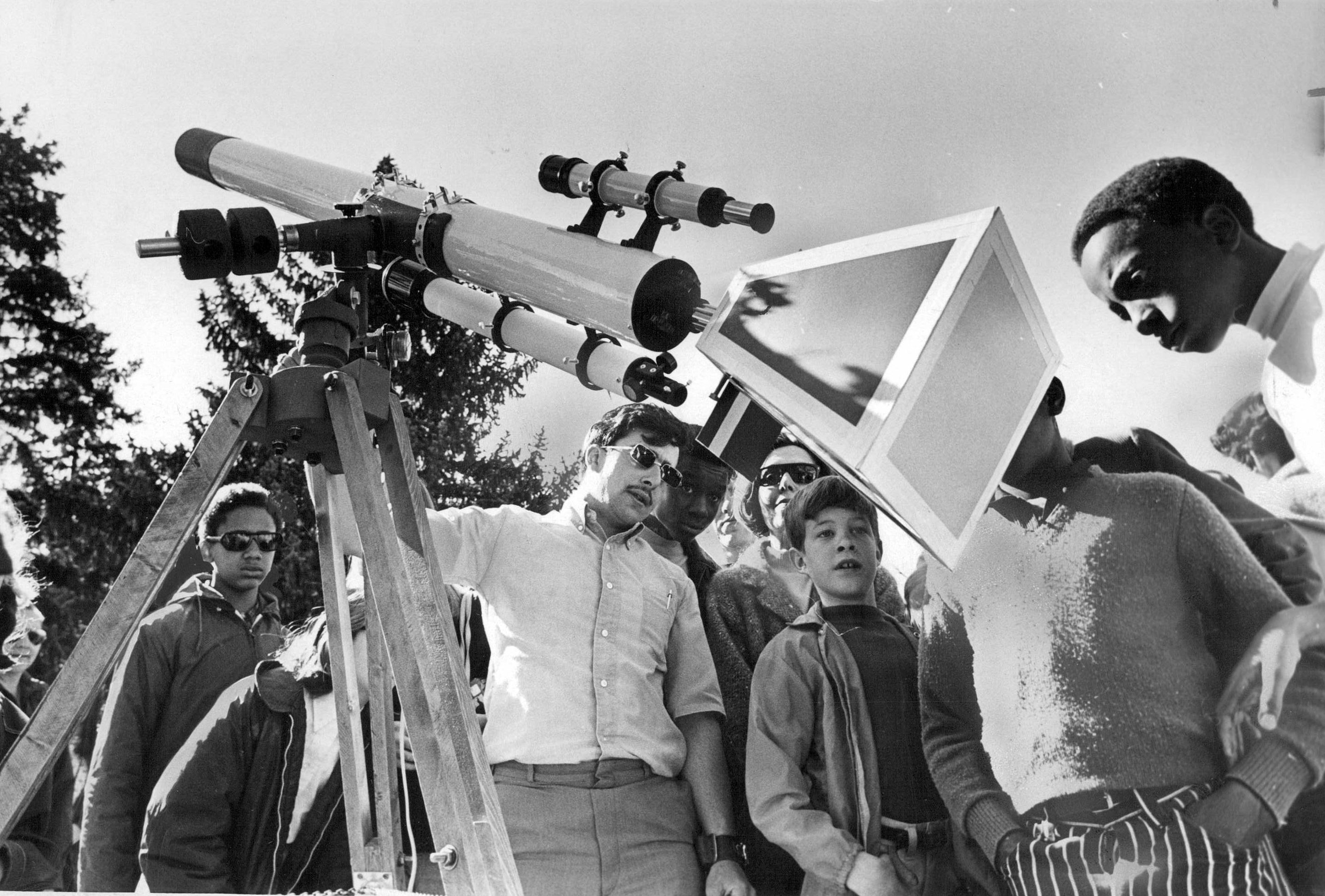 a small group gathers around a projection screen attached to a small telescope pointing at the solar eclipse.