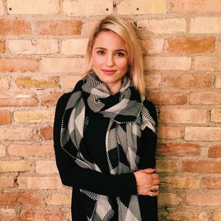 Blond lady smiling wearing black sweater and black and white scarf