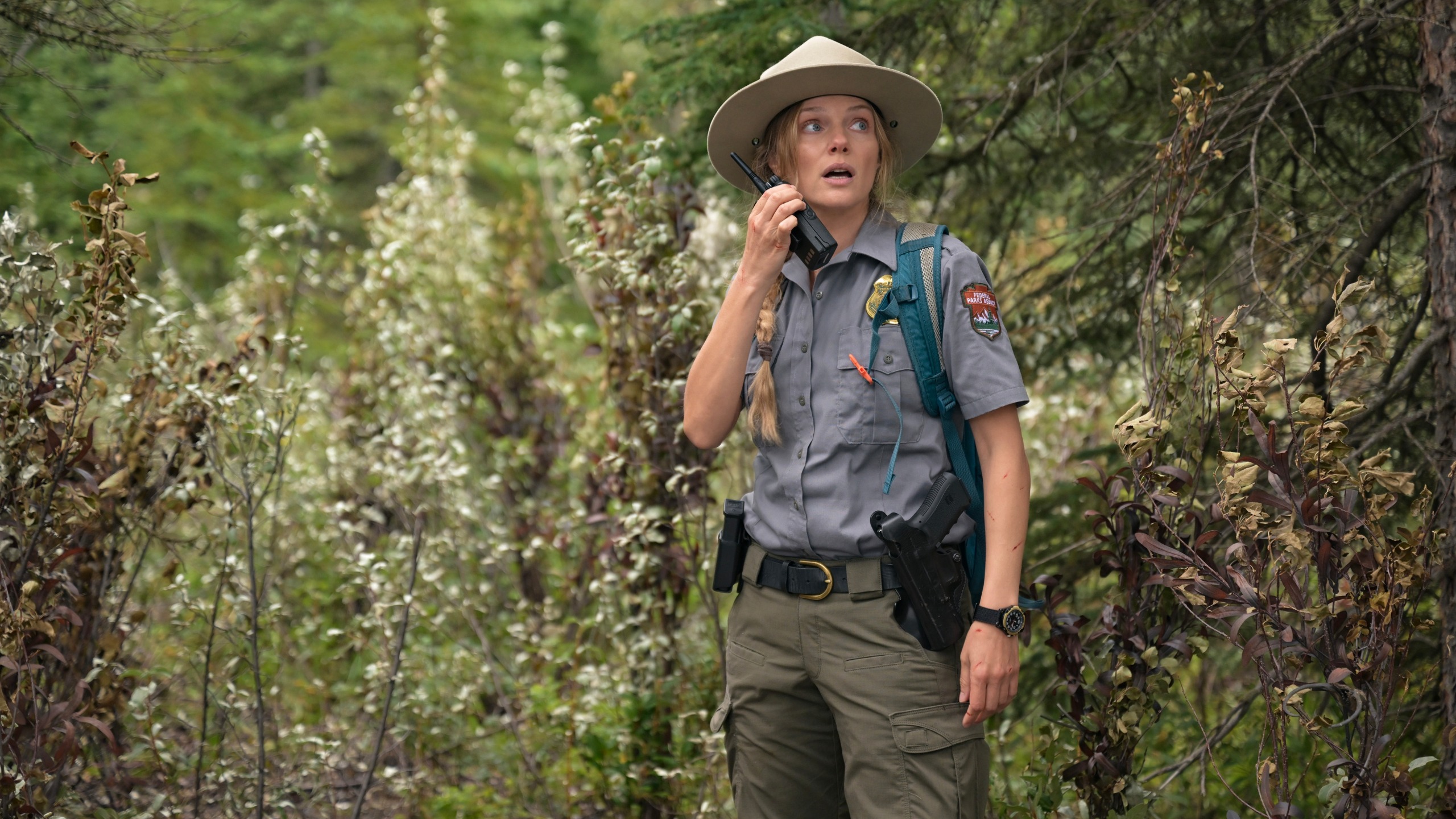 Tracy Spiridakos as Anna Pigeon wearing a National Park ranger uniform looking up at something while on a walkie talkie.