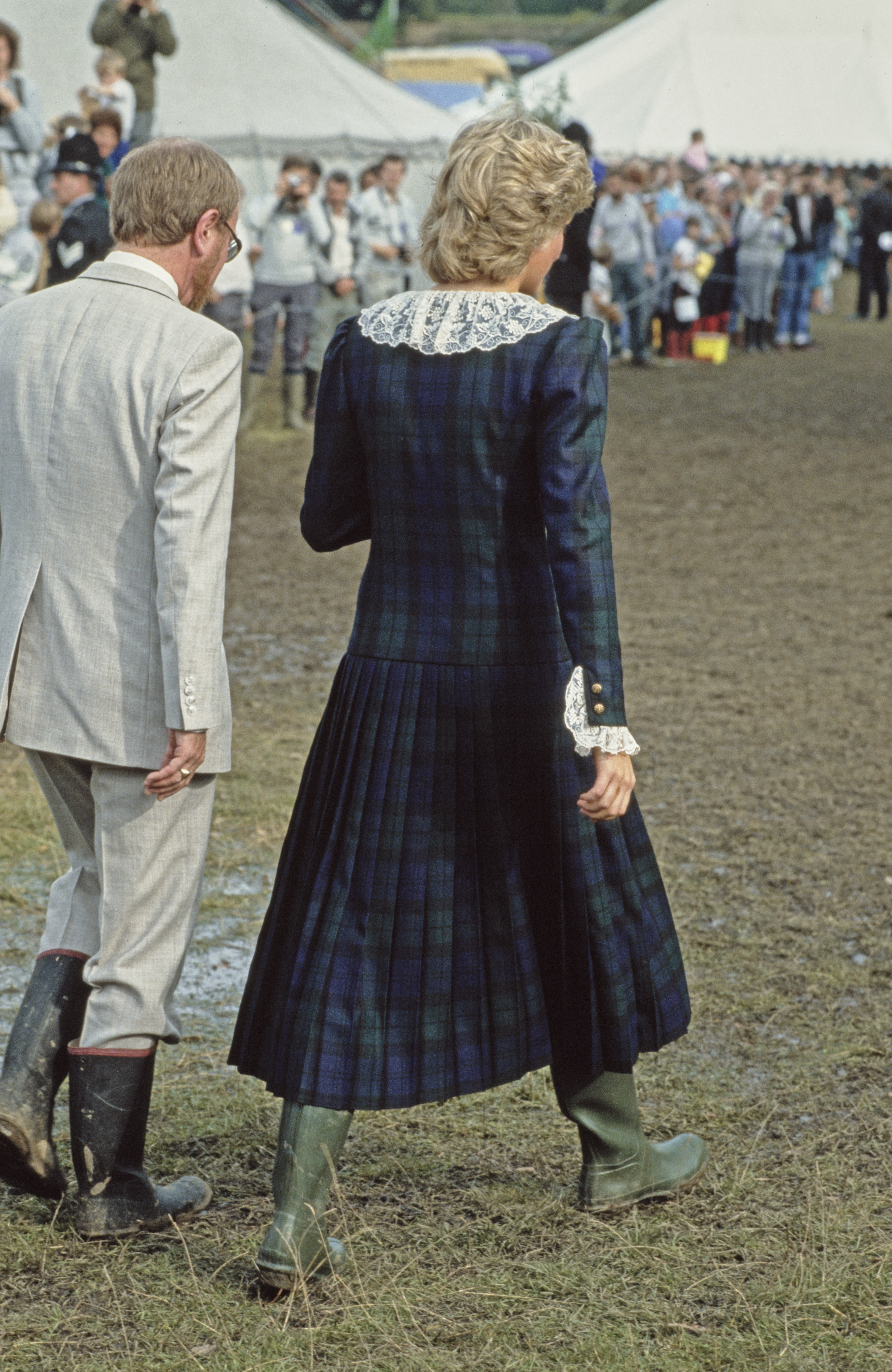 Rear view of British Royal Diana, Princess of Wales wearing a full-length Blackwatch tartan dress with white lace collar and cuffs, with green wellington boots as she attends the Rothesay Highland Games