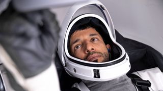 sultan al-neyadi lying in a spacecraft with spacesuit visor open. in front, his blurry hand reaches for a switch