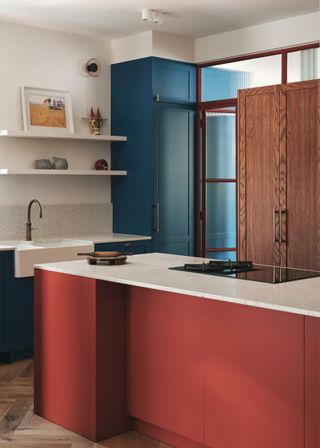 Red lower kitchen cabinets with bright white countertops. Open shelves have been fixed into the kitchen too with a large blue cabinet on the side.