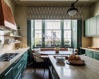 kitchen with dark green cabinets, wood countertops, large window with round dining table and two chairs