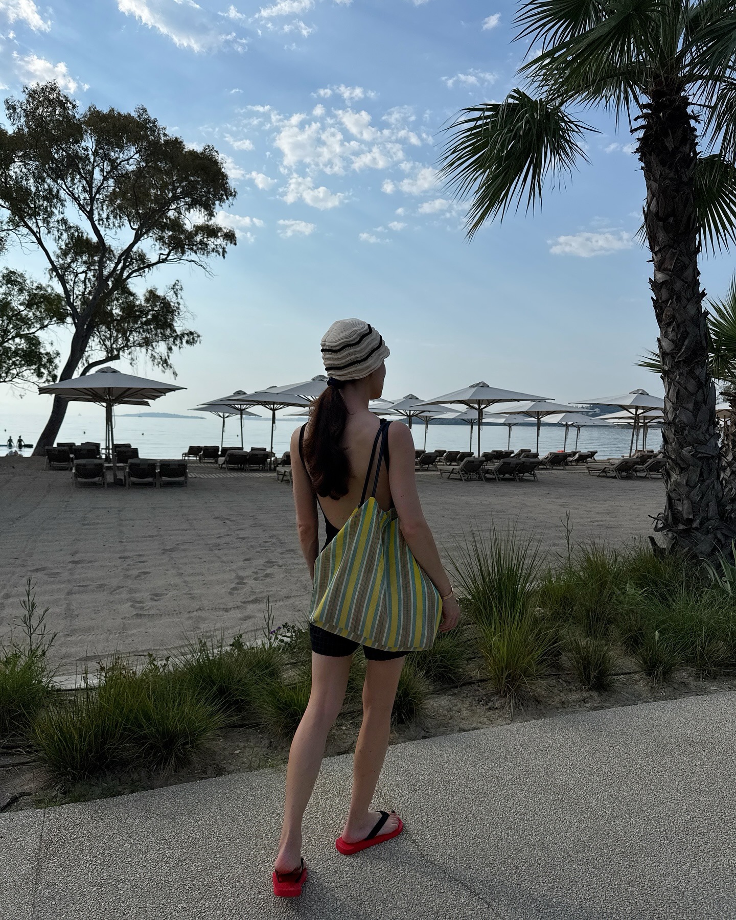 Influencer @annabelrosendahl walks outside by a beach wearing The Row ban bag with a swim suit and red flip-flops.