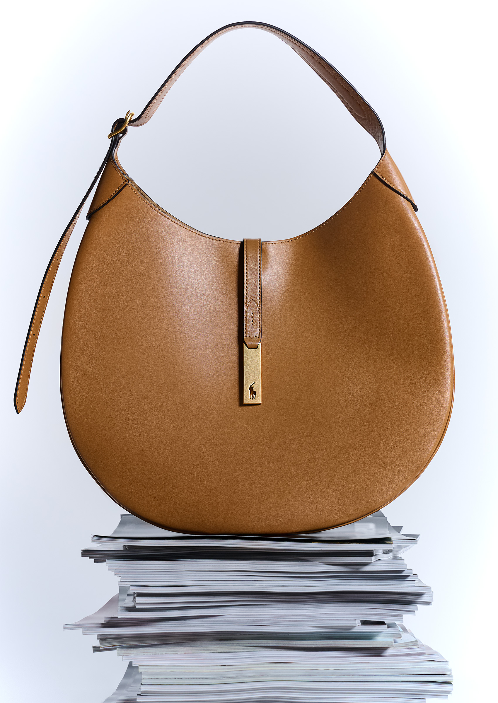 A tan Polo Ralph Lauren bag on a stack of magazines in front of a white background