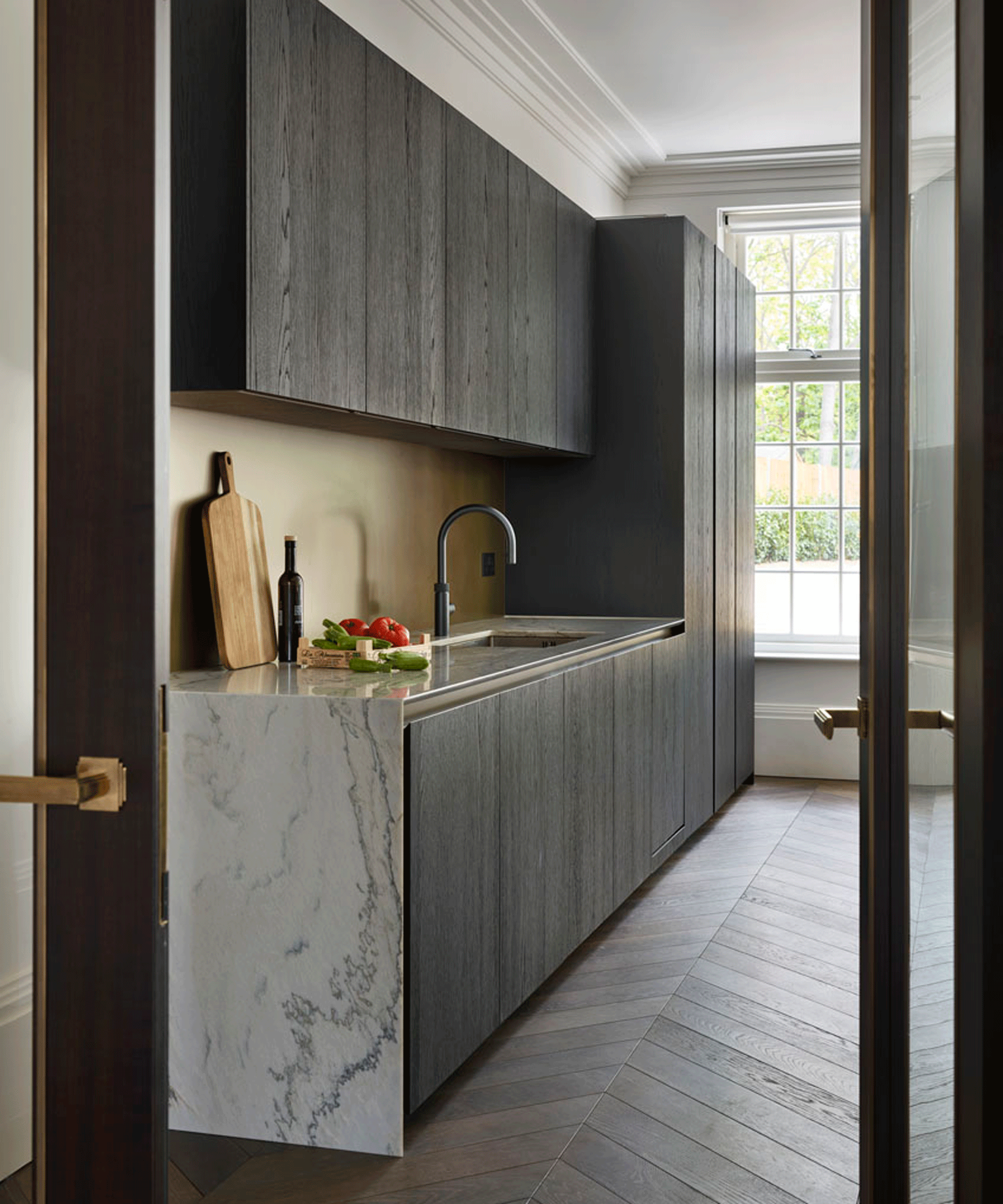 Kitchen with dark cabinetry and marble worktop falling into a waterfall design