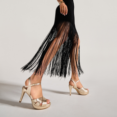 A woman wearing a pair of gold, heeled sandals from Calla Shoes.