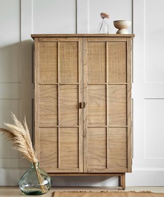 A wooden wardrobe with a glass vase with pampas grass in front of it