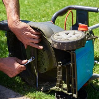 A lawn mower tipped on its side, with someone removing the blade