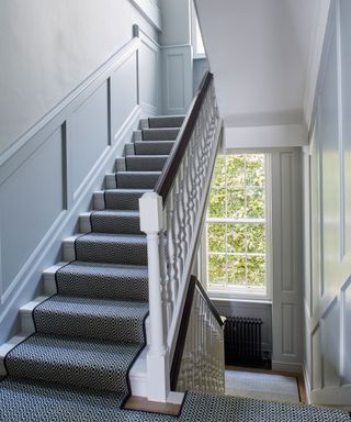 white stairway with light painted blue paneling, black and white stair runner, black radiator