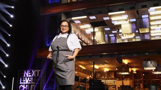 Contestant Tia in white top and grey apron in front of kitchen in Next Level Chef.