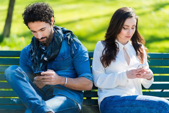 A couple looks down at their cell phones.