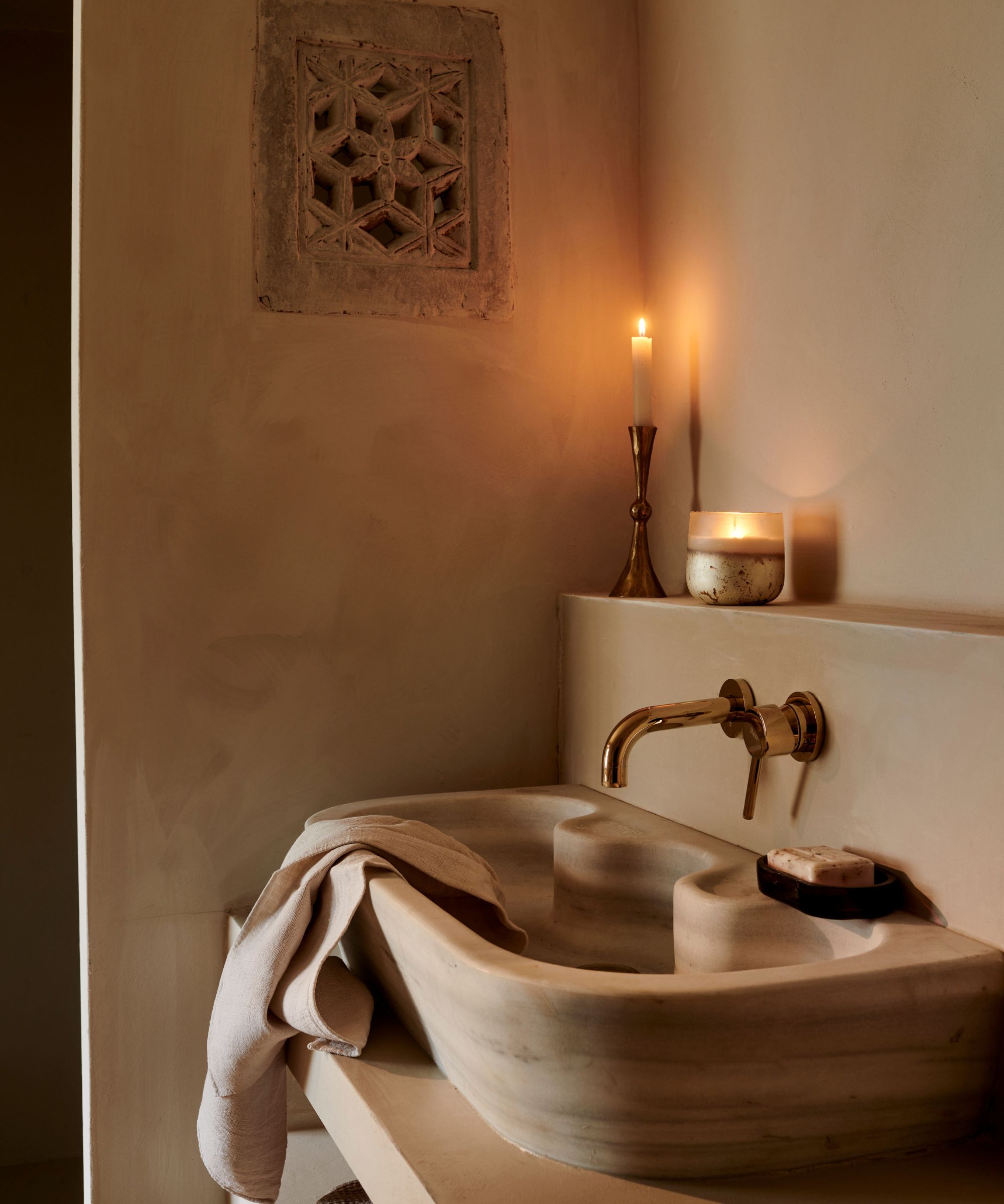 A carved stone sink in a paster-wall bathroom. A candle lit on the ledge above.