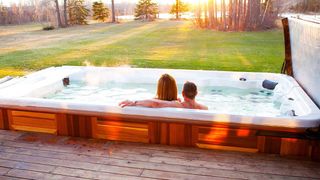 Arctic Spas review: A man and a woman sit in the Wolverine Pool enjoying the view of a nearby lake