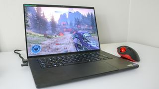 The GameBall Thumb trackball mouse next to a gaming laptop running Halo Infinite
