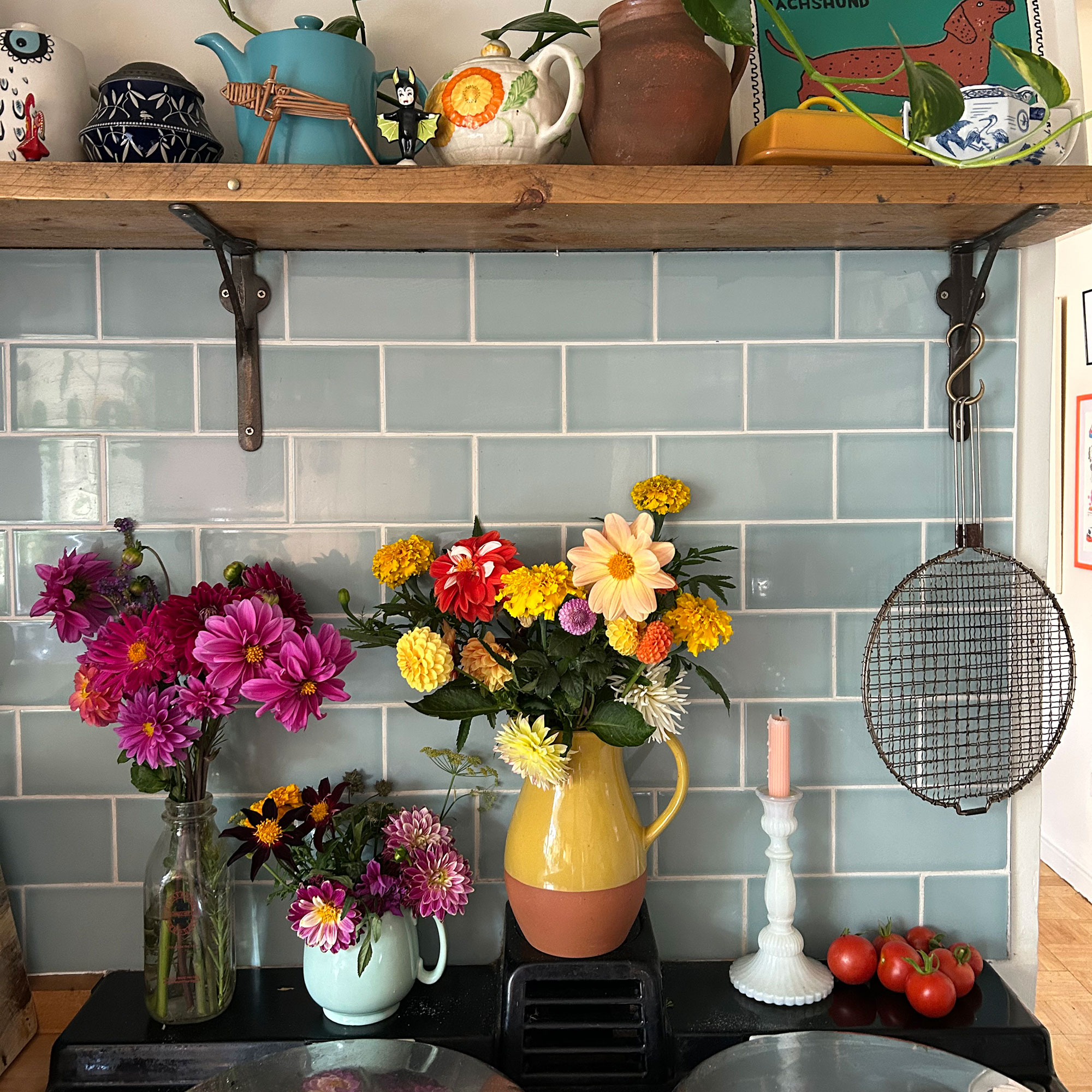 Three jugs of mixed colourful flowers on top of AGA range cooker in front of pale blue tiled splashback