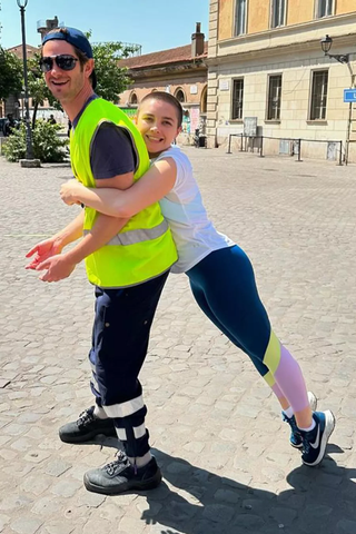 Florence Pugh wearing leggings and a tshirt hugging Andrew Garfield, who is wearing a neon visibility vest, from the back