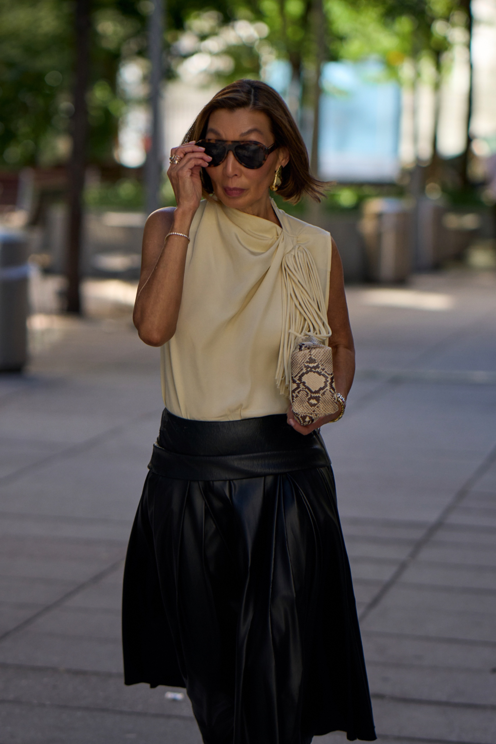A woman wearing sunglasses, a yellow top and black skirt caught on the street at New York Fashion Week
