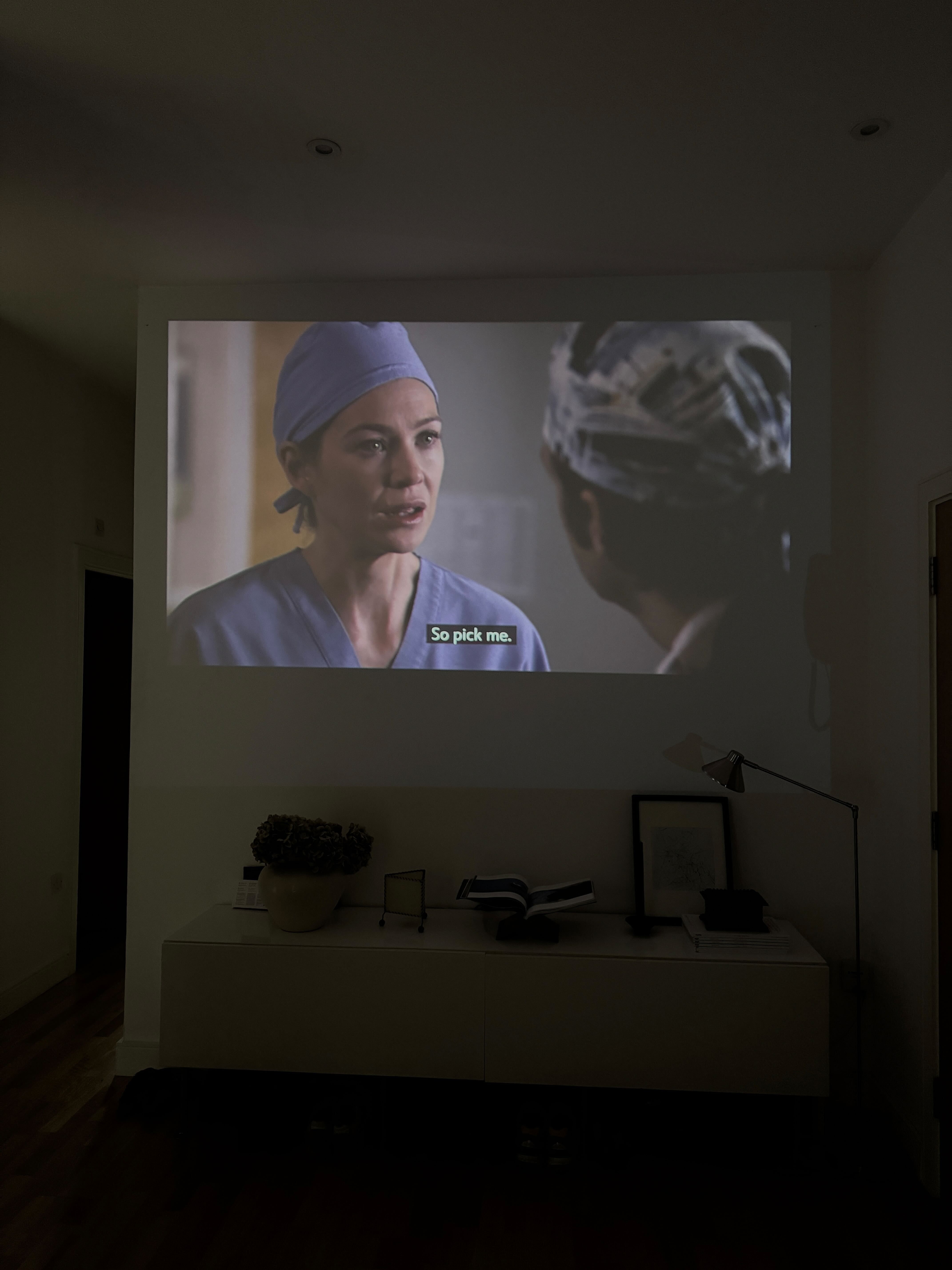 scene from grey&#039;s anatomy with meredith grey projected onto a wall with the subtitles &quot;pick me&quot;