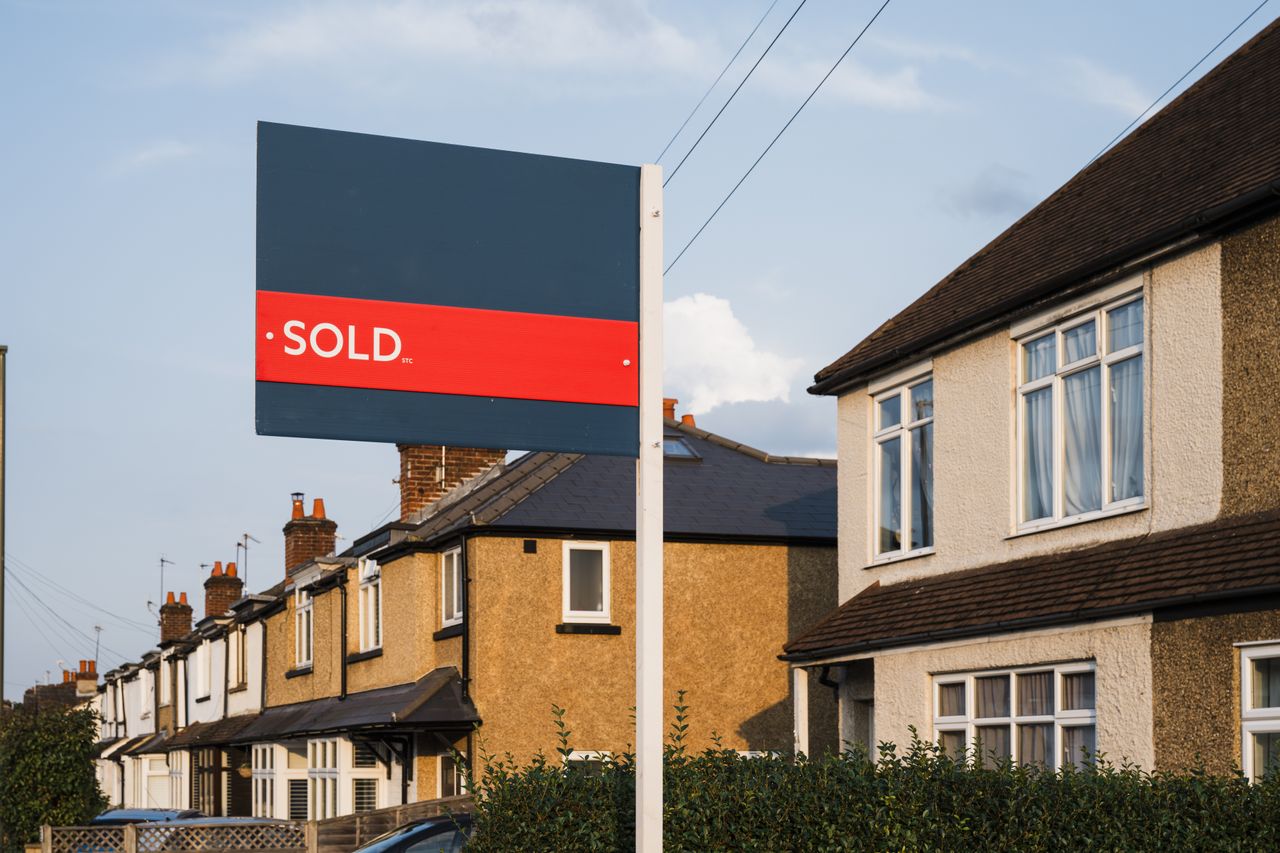 House for sale sign with &quot;sold&quot; banner on it in front of houses in residential area