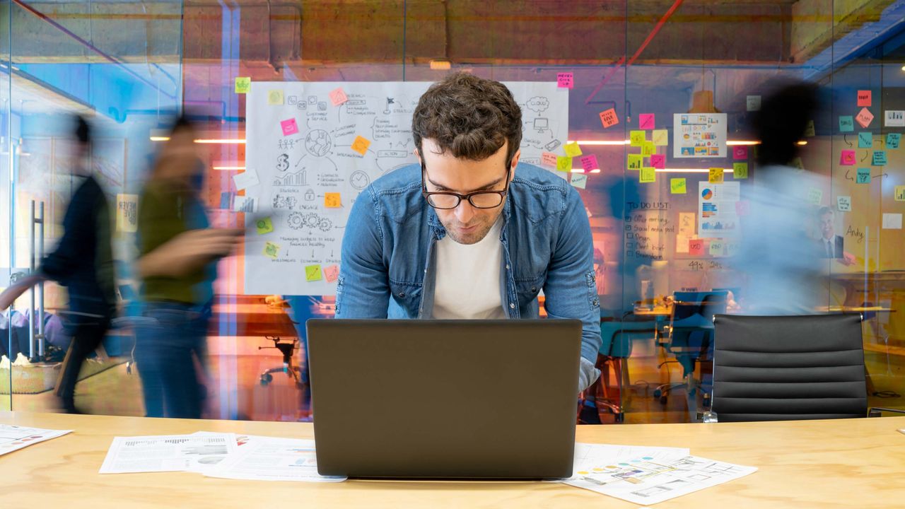 A small businessman peers at his computer as busy people walk all around him.