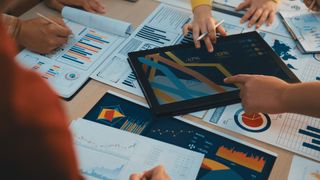 A diverse business team engages in collaborative work, analyzing charts and reports while using a digital tablet to drive strategic decisions in a modern office setting