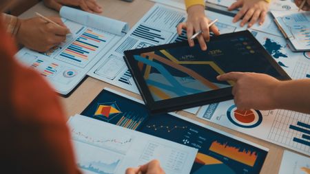 A diverse business team engages in collaborative work, analyzing charts and reports while using a digital tablet to drive strategic decisions in a modern office setting