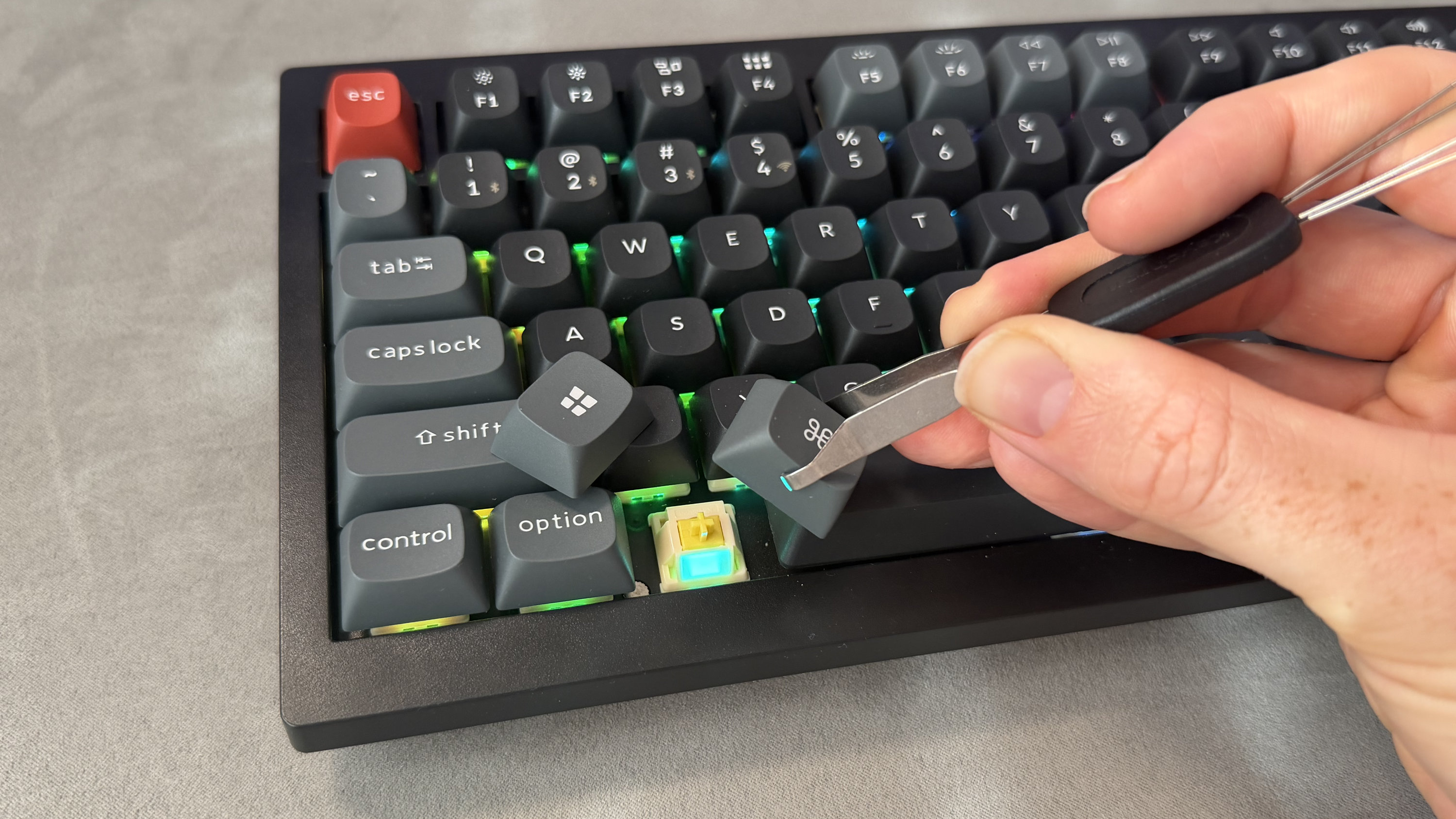 A man's hand using a key removal tool to replace the Windows key cap of the Keychron V1 Ultra 8K with a Command key cap.