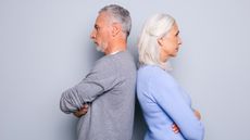 An older man and woman stand back to back with their arms crossed, clearly unhappy.
