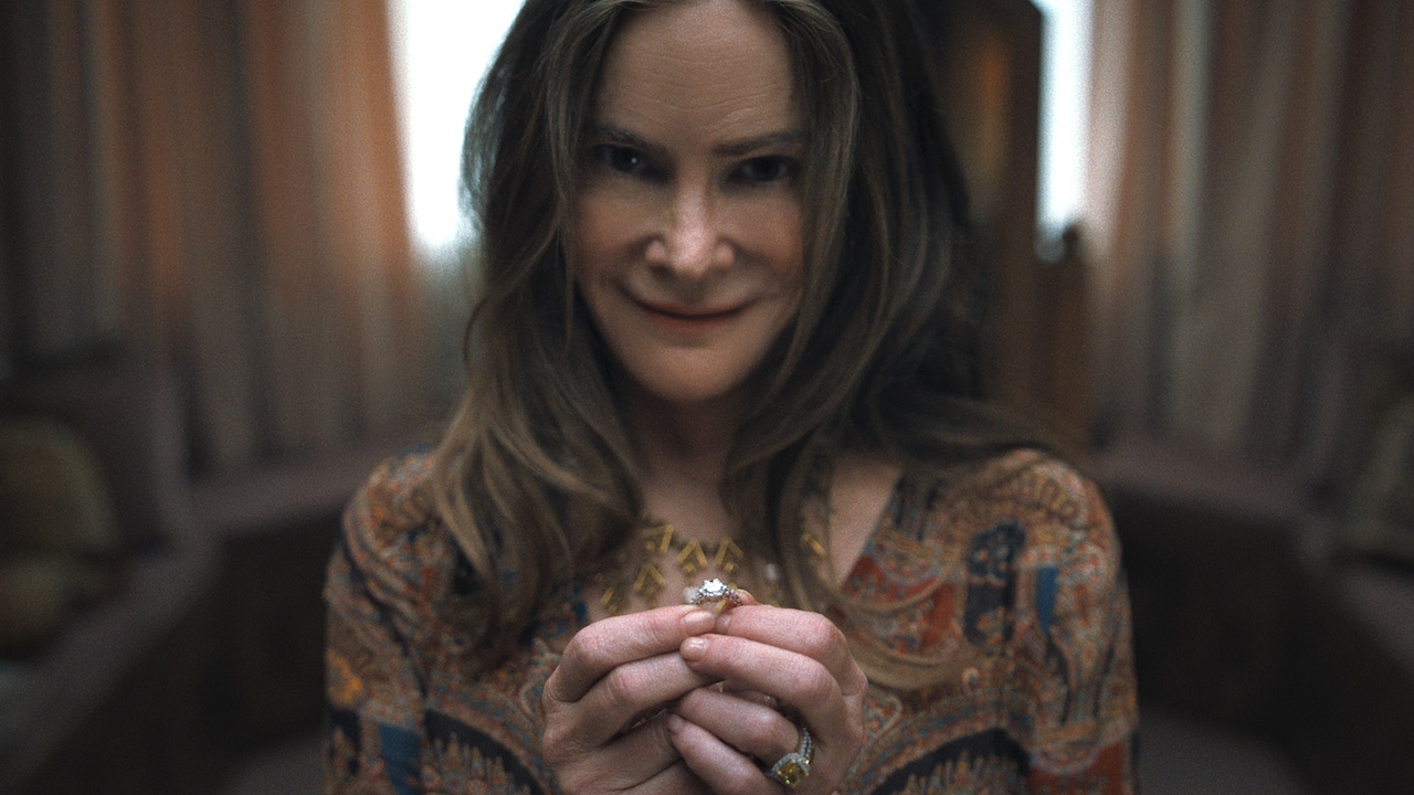 Jennifer Jason Leigh flashing a creepy smile while holding a wedding ring in Something Very Bad Is Going To Happen