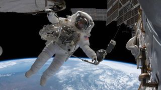 astronaut in a spacesuit backdropped by earth. pieces and solar panels of the space station are visible around him