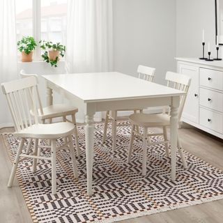 A scandinavian weave rug in white, red, and black with a white wooden table and chairs on top