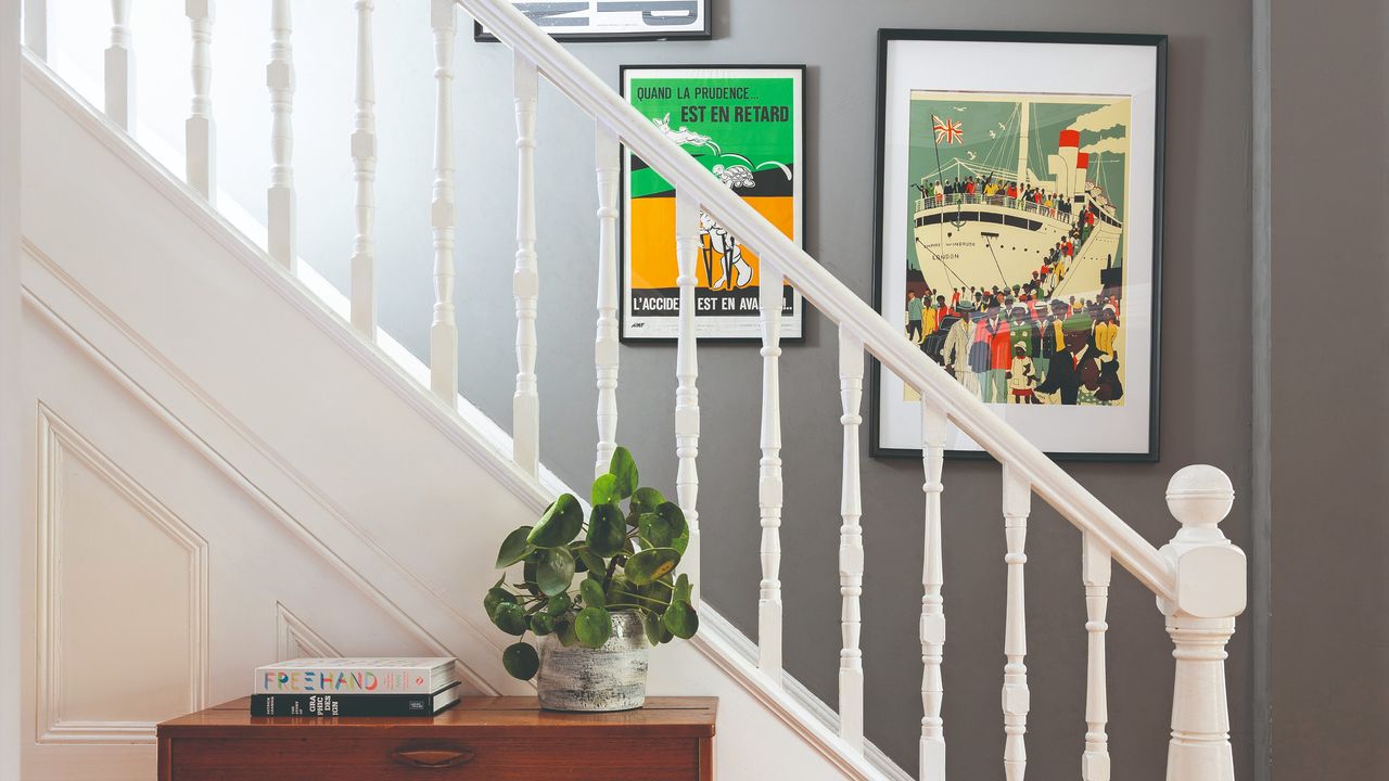 A staircase with white railing and bannister paired with grey-painted walls with a gallery wall display