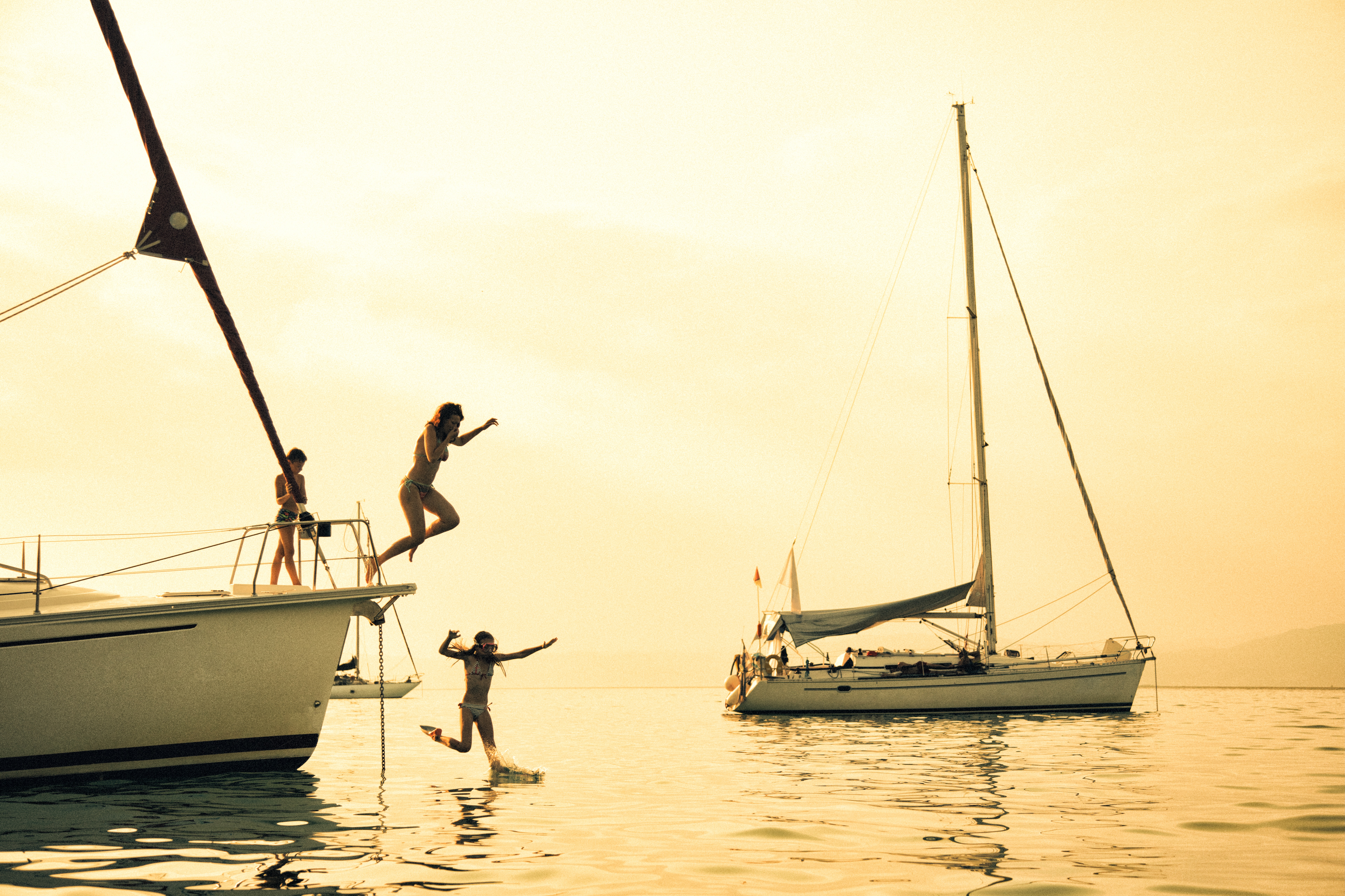 Three children diving into the sea from the deck of a sailing boat