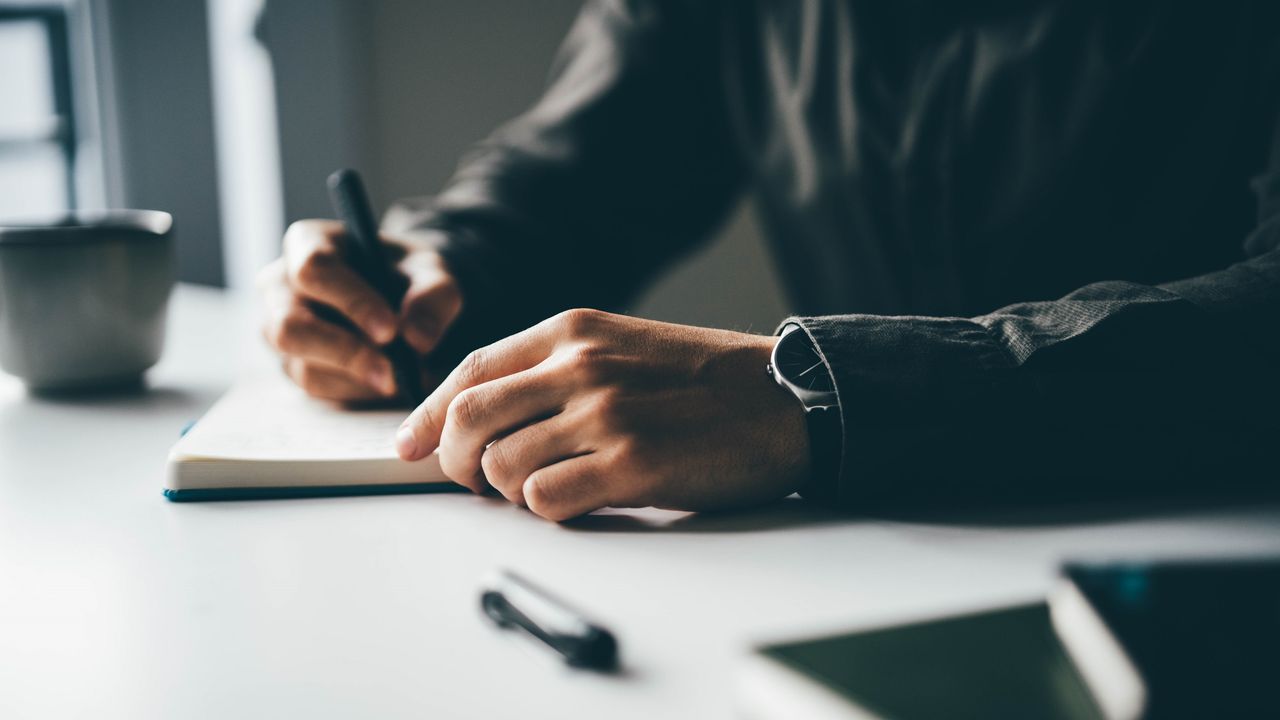 A man writes in a notebook at his desk.