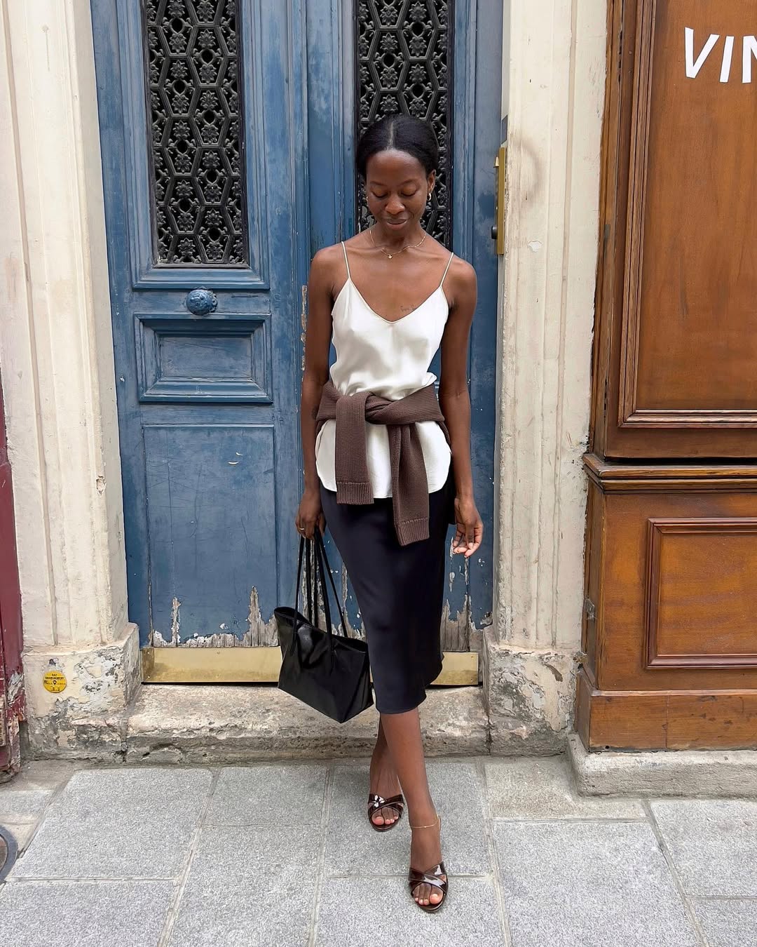 @sylviemus_ wears a black satin skirt with a white camisole and mules
