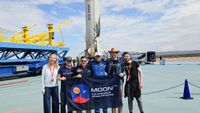 six people stand in front of a white rocket booster on a landing pad, holding a blue sign that reads "moondao"