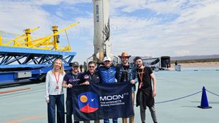 six people stand in front of a white rocket booster on a landing pad, holding a blue sign that reads &quot;moondao&quot;