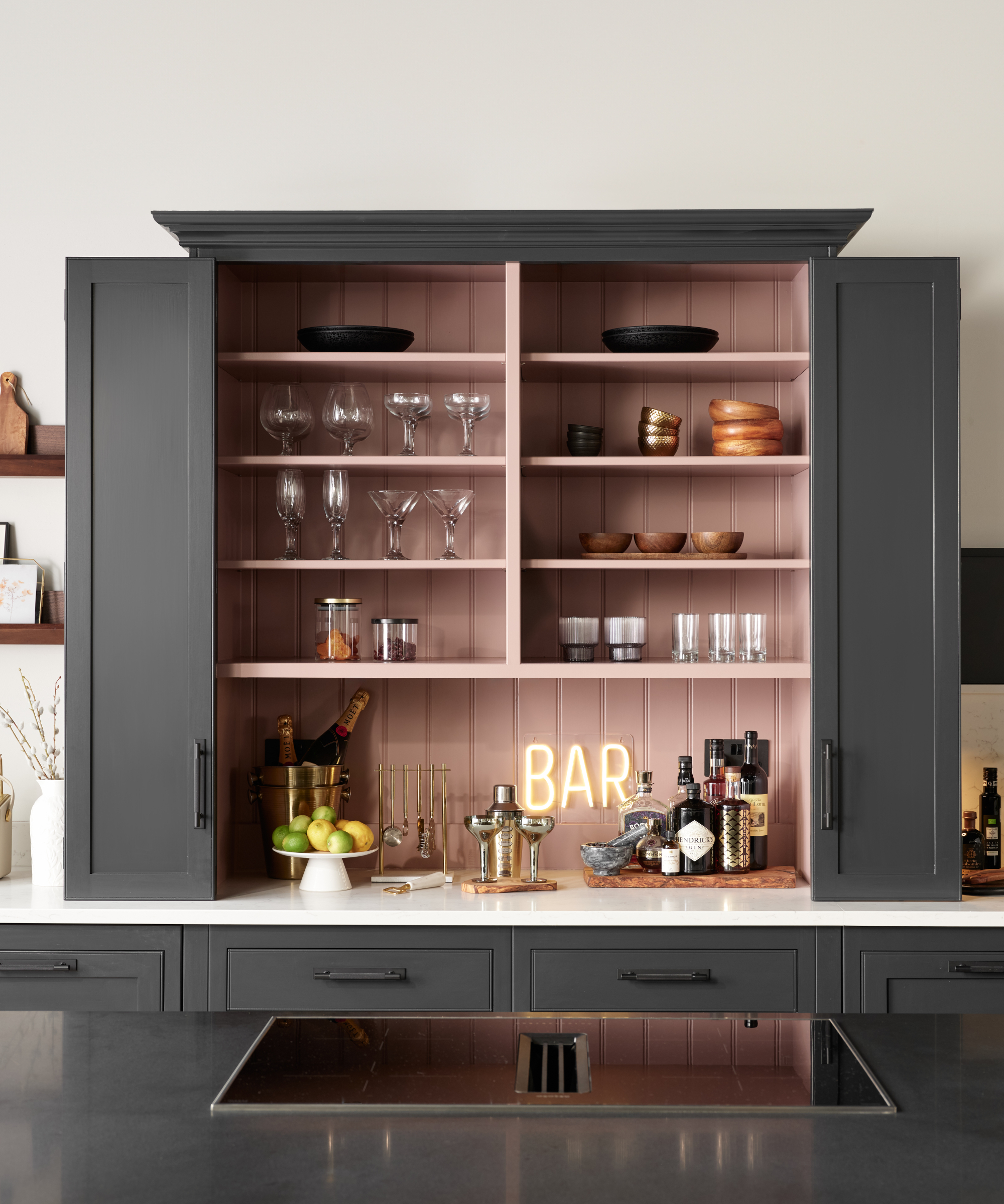 grey kitchen cabinets above worktop opened to reveal pink interior and bar on prep area