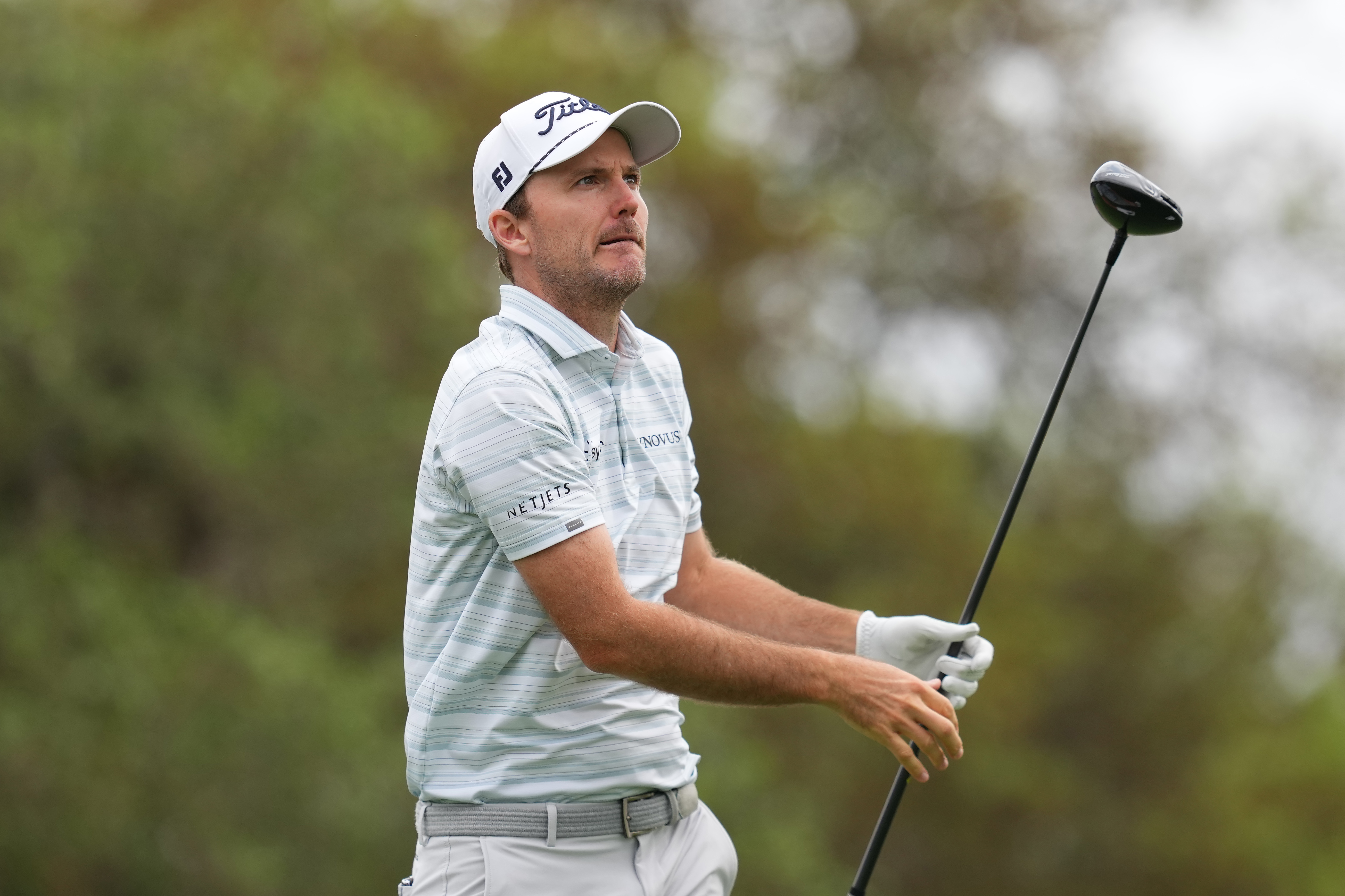 Russell Henley watches a tee shot with a driver in hand