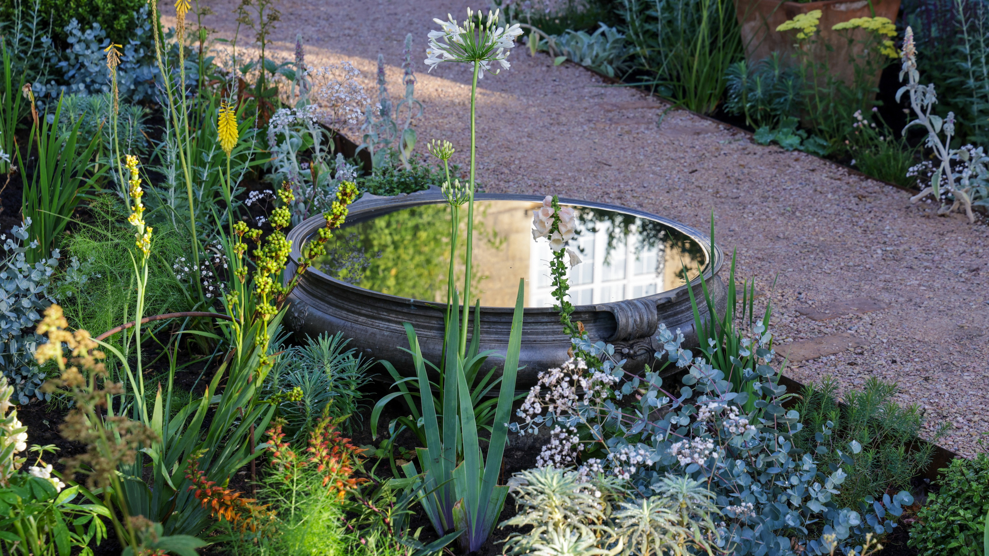 small water feature beside a garden path surrounded by flowers and plants