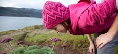 A young girl dressed in pink smells the spring flowers, while out hiking.