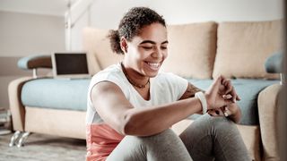 Woman sitting on the floor of her living room looks at her fitness tracker