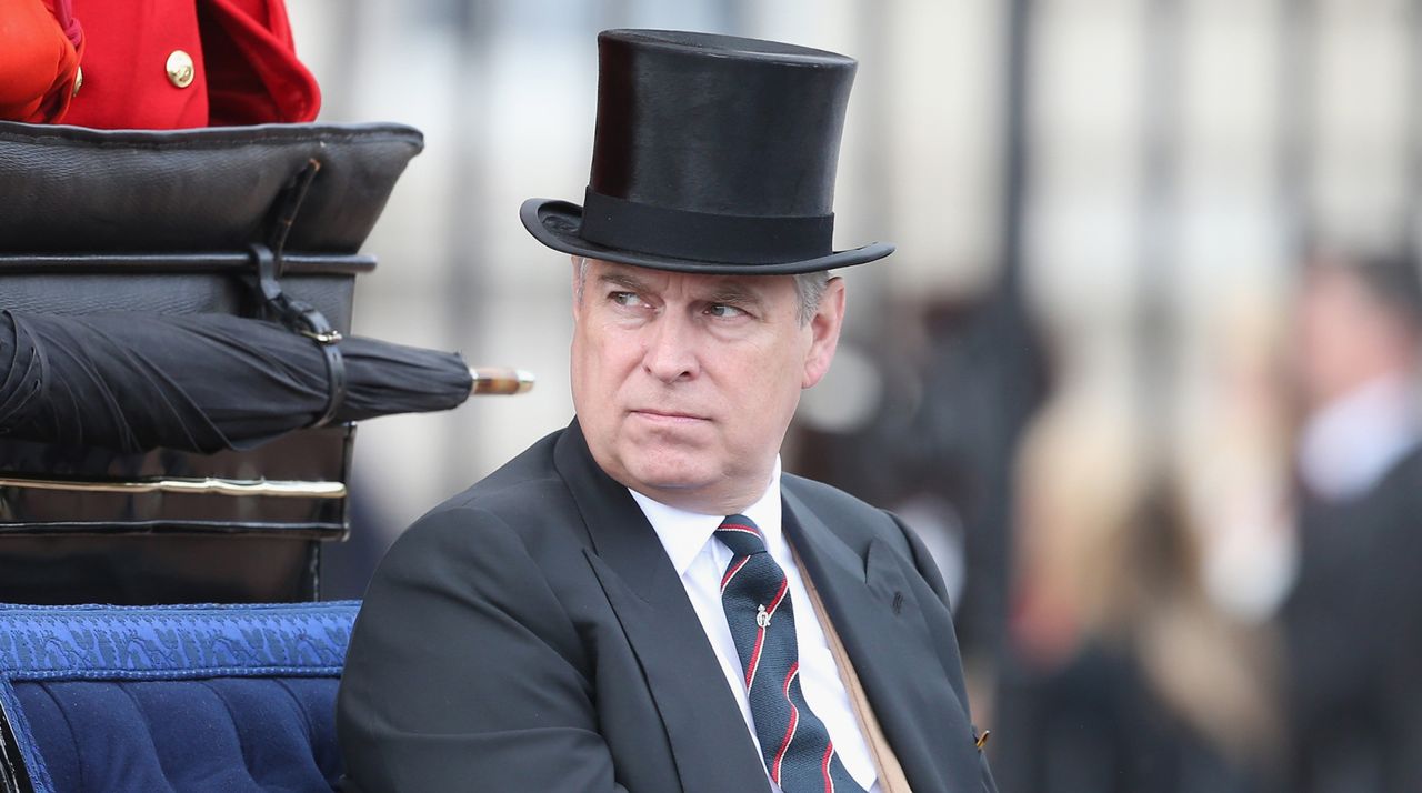 Prince Andrew rides in a carriage while wearing a top hat and a suit