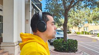 1More SonoFlow SE headphones worn by reviewer standing outdoors on a street