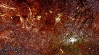 A panorama shows glowing reddish gas mixed with stars in deep space