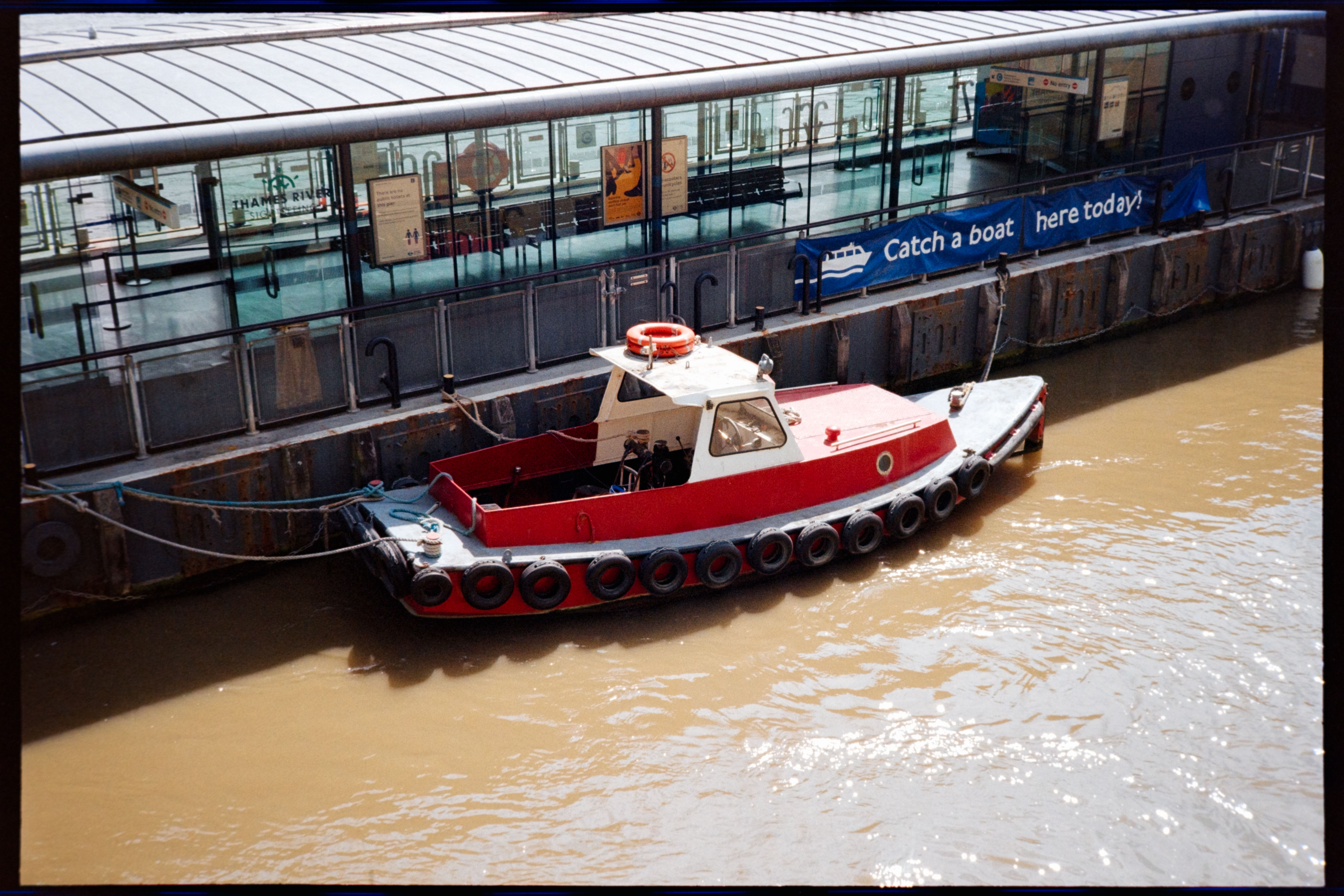A red and white boat moored beside the Thames River pier in London.