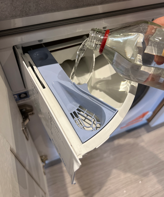 A washing machine detergent dispenser being filled with vinegar