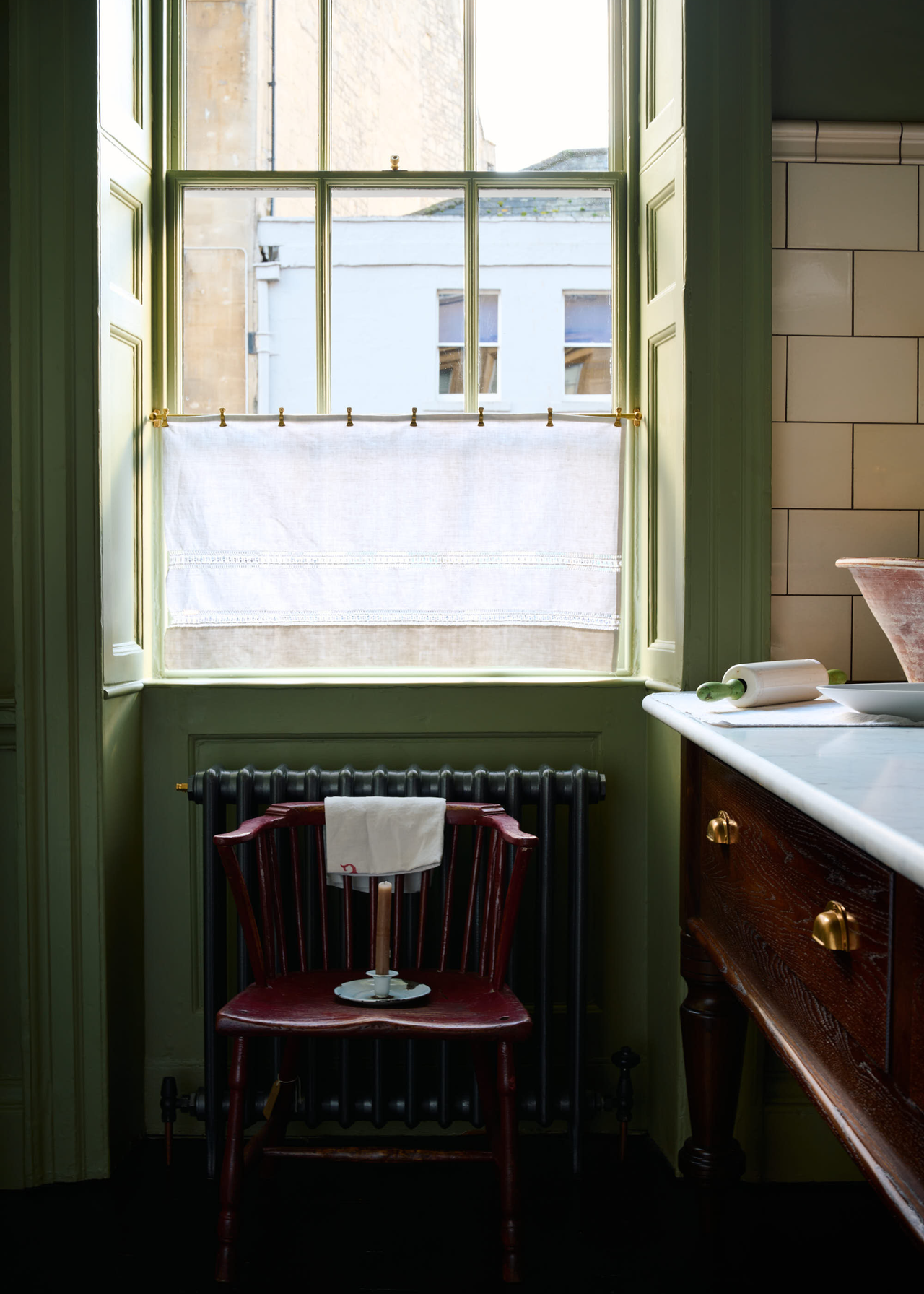 small kitchen with green walls and wooden details and a cafe curtain