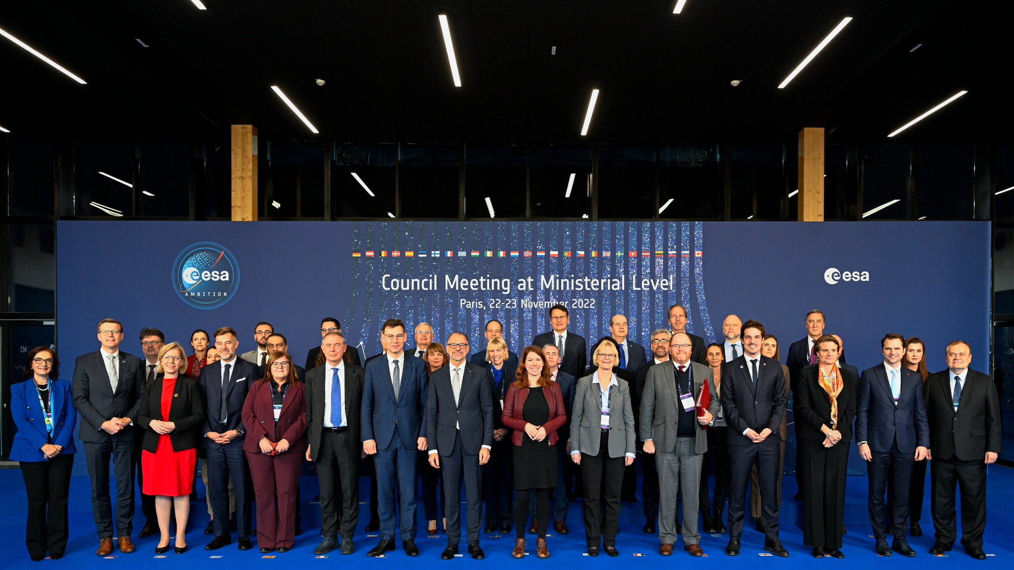 several dozen well-dressed people stand in front of a blue backdrop at a conference